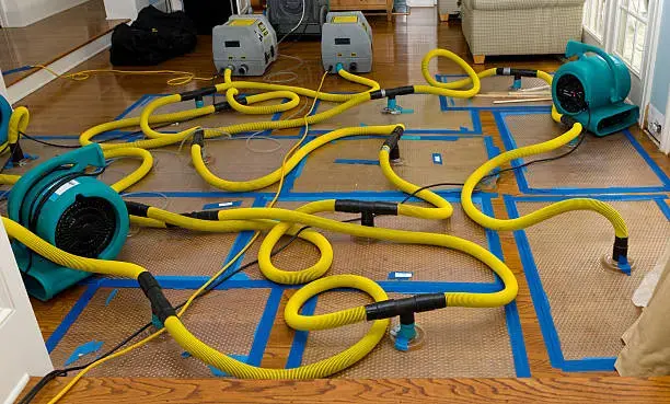 Floor drying mats and hoses pulling water out of hardwood in a Fontana home