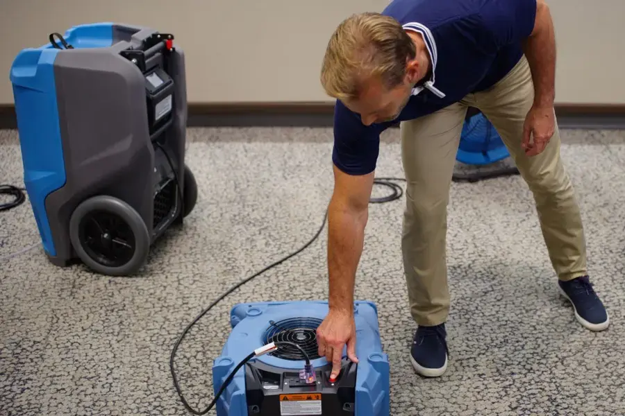 Tech setting an air mover beside an LGR dehumidifier to dry a wet carpet in a Fontana home