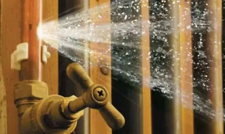 Water spraying from a burst supply pipe inside an open wall in Fontana