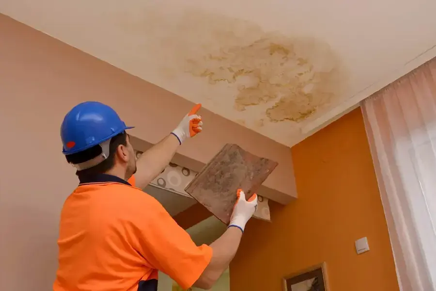 Tech in a hard hat inspecting a roof leak stain on a Fontana ceiling